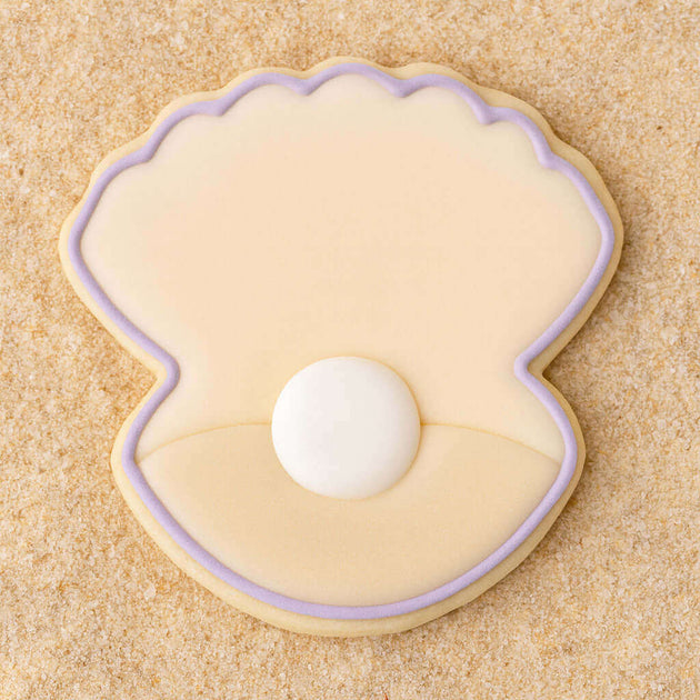 Clam shell with pearl  outlined in purple cookie on a sandy background from a 4 inch Oyster Clam Shell Metal Cookie Cutter
