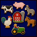 A set of six farm-themed sugar cookies decorated with icing and arranged on a dark blue background. The cookies include a black-and-white cow, a pink pig, a gray donkey, a red barn with a silo, a white rooster with colorful tail feathers, and a green tractor with a farmer driving it from a Set of Farm Metal Cookie Cutters