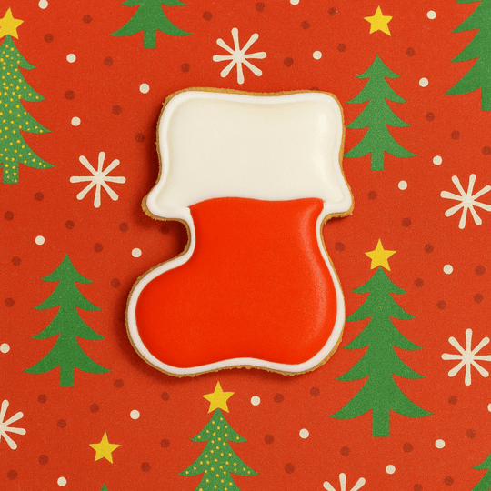 Red and white Christmas stocking cookie on a festive background with trees and stars.