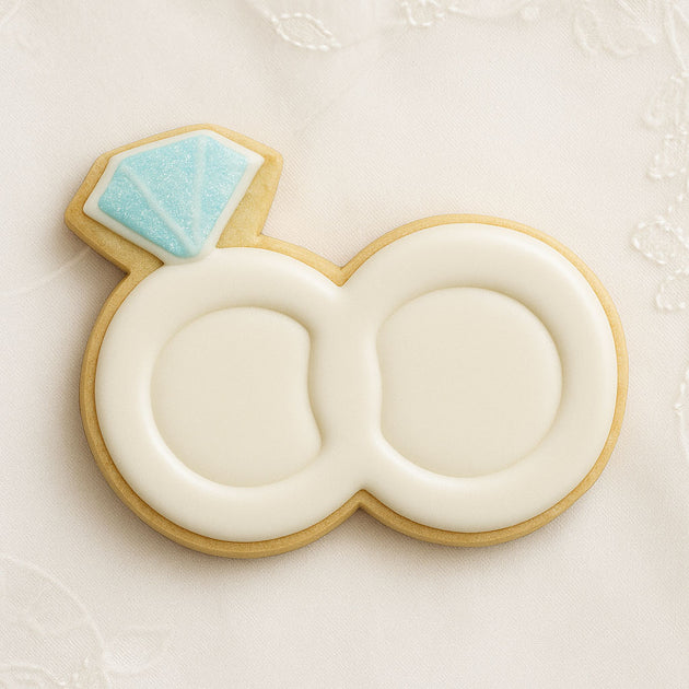 Cookie shaped like a wedding ring with a blue gemstone on a white background from a 1.75 inch Mini Double Wedding Rings Metal Cookie Cutter