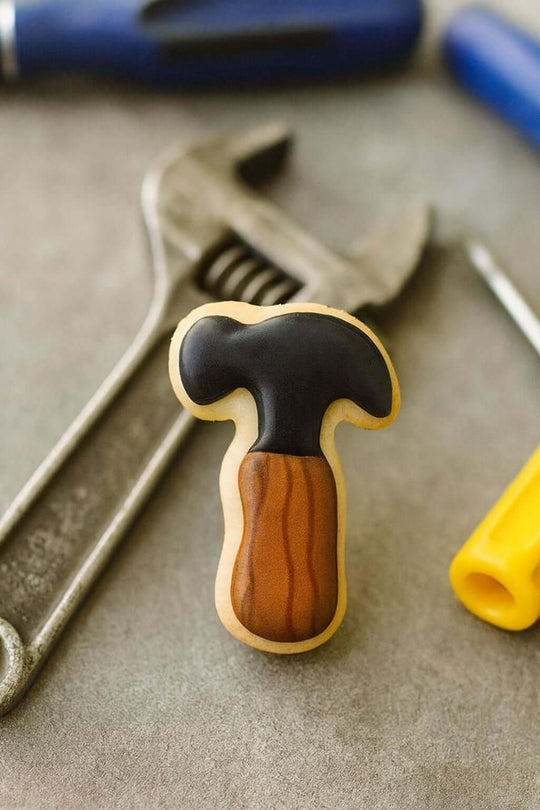 Cookie with a hammer design on a surface with tools in the background from a 2 inch Mini Hammer Metal Cookie Cutter