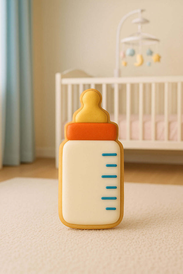 Baby bottle-shaped toy on a light-colored surface with a crib and mobile in the background from a 2 inch mini baby bottle metal cookie cutter.