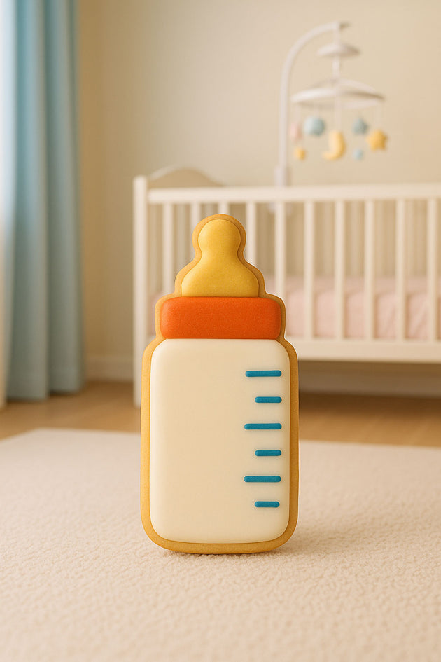 Baby bottle-shaped toy on a light-colored surface with a crib and mobile in the background from a 2 inch mini baby bottle metal cookie cutter.