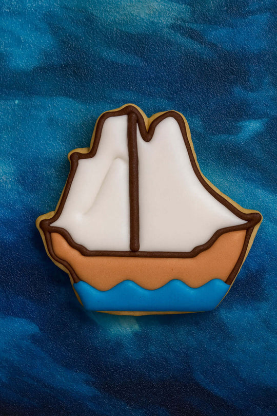 Decorative cookie shaped like a sailboat on a blue textured background