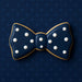 Navy blue bow tie cookie with white dots on a dark blue polka dot background from a 1.75 inch Mini Bow Tie Metal Cookie Cutter
