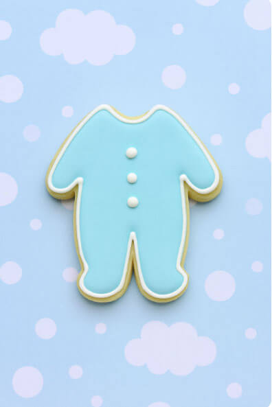Cookie shaped like a baby footie pajamas on a light blue background with white dots from a  2 inch Mini Footie Pajamas Metal Cookie Cutter