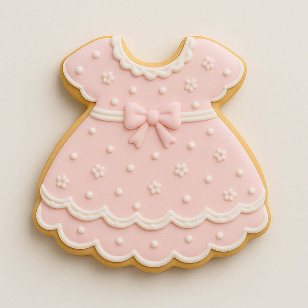 Cookie shaped like a pink dress with white details on a light beige background from a 2 inch Mini Baby Dress Metal Cookie Cutter 