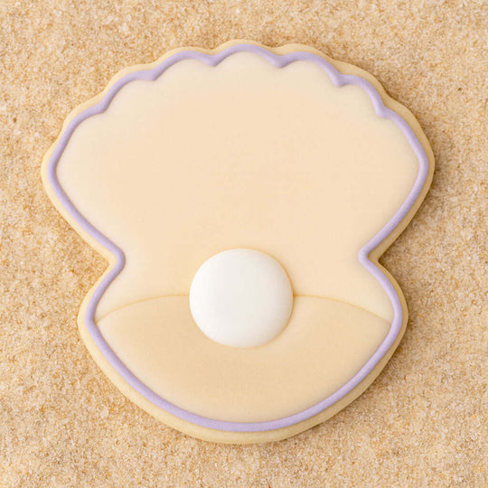 Cookie shaped like a seashell with a pearl on a sandy background from a 2 inch Mini Oyster Clam Shell with Pearl Metal Cookie Cutter