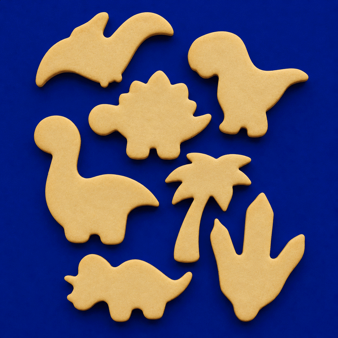 Set of beige dinosaur and palm tree cookie cutters on a blue background from a Set of Dinosaur Metal Cookie Cutters