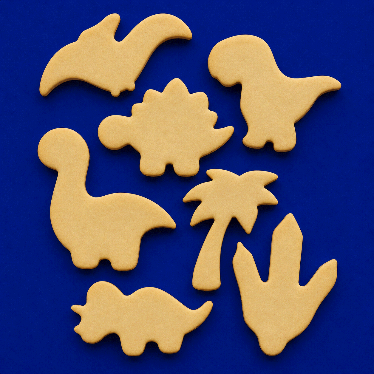 Set of beige dinosaur and palm tree cookie cutters on a blue background from a Set of Dinosaur Metal Cookie Cutters