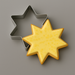 A metal star-shaped cookie cutter next to a yellow iced star-shaped cookie on a smooth gray surface from 3.5 inch Star of Bethlehem Moravian Star Metal Cookie Cutter