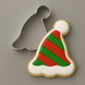 A 3.75 inch Elf Party Ski Hat Metal Cookie Cutter shown next to a decorated sugar cookie shaped like a Santa hat, on a plain gray background.