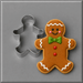 A 2.25 inch Mini Gingerbread Boy Metal Cookie Cutter shown next to a decorated gingerbread man cookie on a smooth gray surface.
