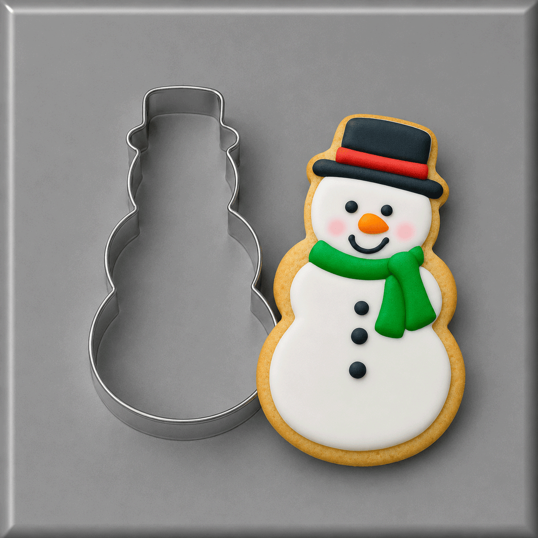 A 4 inch Snowman Metal Cookie Cutter shown next to a decorated snowman cookie on a smooth gray surface.