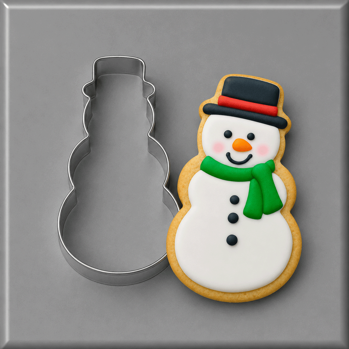 A 4 inch Snowman Metal Cookie Cutter shown next to a decorated snowman cookie on a smooth gray surface.