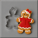 A 3 inch Gingerbread Girl Metal Cookie Cutter shown next to a decorated gingerbread cookie shaped like a girl in a red dress with white icing details, on a gray background.
