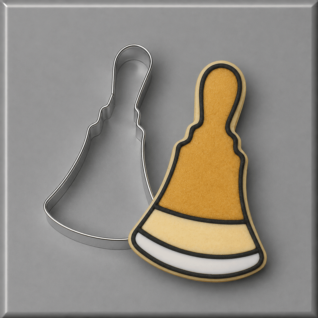 A 3.5 inch Hand Bell Metal Cookie Cutter shown next to a decorated sugar cookie in the same bell shape, on a smooth gray background.