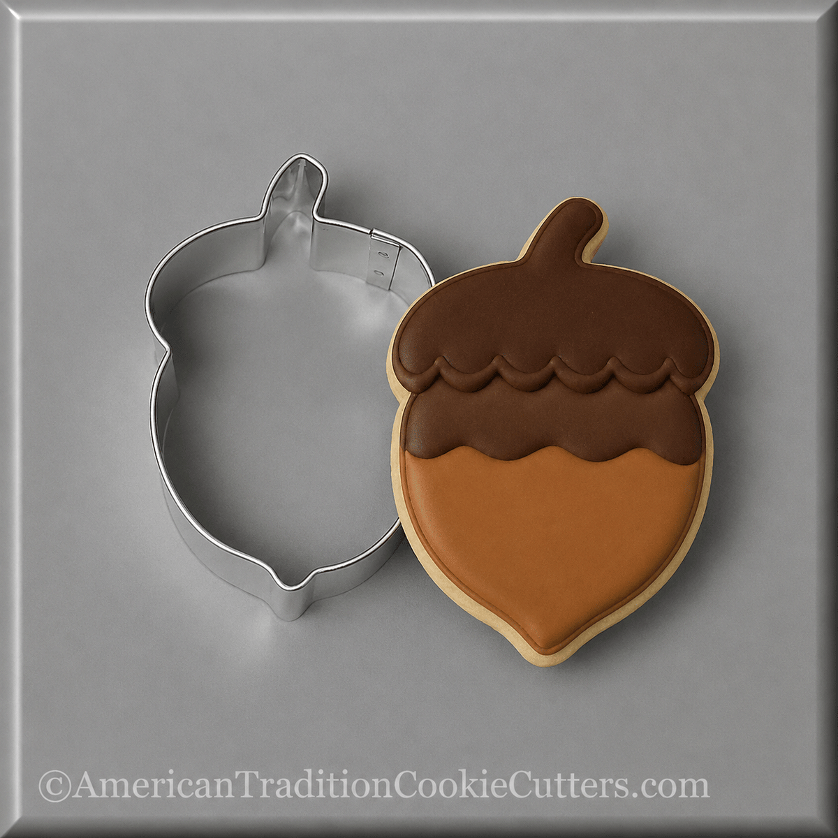 A 3 inch Acorn Metal Cookie Cutter shown next to a decorated acorn-shaped sugar cookie on a neutral gray background.