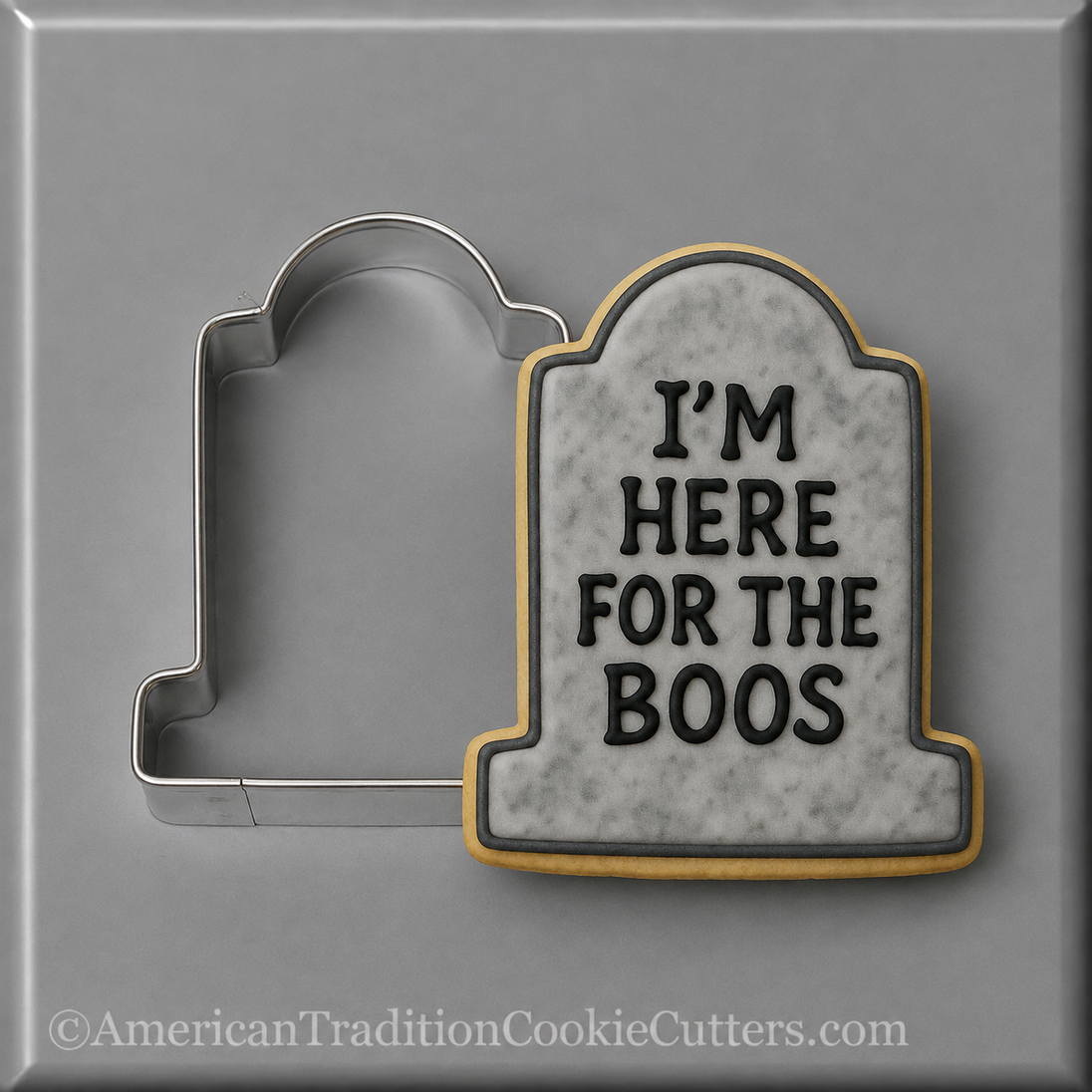 A 3 inch Tombstone Metal Cookie Cutter shown next to a decorated tombstone-shaped cookie on a gray background. The cookie has a gray marble-look center with black text reading 'I'M HERE FOR THE BOOS' and a gold border.