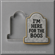 A 3 inch Tombstone Metal Cookie Cutter shown next to a decorated tombstone-shaped cookie on a gray background. The cookie has a gray marble-look center with black text reading 'I'M HERE FOR THE BOOS' and a gold border.