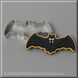 A 4.5 inch Flying Bat Metal Cookie Cutter shown with a decorated bat-shaped cookie underneath on a gray background. The cookie is black with white eyes, white fangs, and a gold outline.