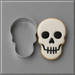A 3 inch Skull Metal Cookie Cutter shown next to a decorated sugar skull cookie with white icing, black details, and a golden-brown edge, on a gray background.