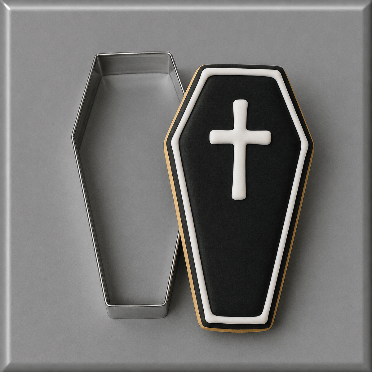 A coffin-shaped cookie with black icing, a white cross, and white border trim, shown next to a 4 inch Coffin Metal Cookie Cutter on a gray background.
