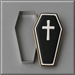 A coffin-shaped cookie with black icing, a white cross, and white border trim, shown next to a 4 inch Coffin Metal Cookie Cutter on a gray background.
