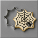 A star-shaped sugar cookie decorated with a black spiderweb pattern and a small gray-and-black spider, shown next to a matching 3 inch Spider Web Metal Cookie Cutter on a smooth gray background.