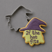 A 4 inch Witch Head Metal Cookie Cutter is shown beside a decorated sugar cookie in the shape of a witch hat with the phrase 'If the hat fits' in purple icing, on a smooth gray background.