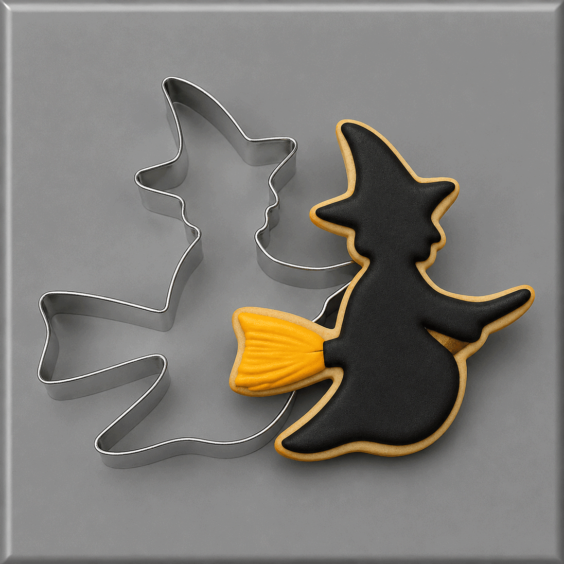 A Halloween-themed cookie cutter set on a gray background, featuring a witch silhouette cutter with a black and yellow decorated cookie inside, and a 3.75 inch Flying Witch Metal Cookie Cutter behind it.
