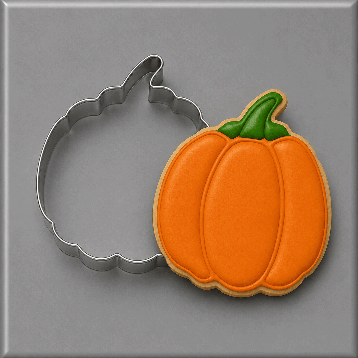 A 4 inch Pumpkin Metal Cookie Cutter shown next to a decorated pumpkin-shaped cookie with orange icing and a green stem, on a gray background.
