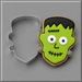 A Frankenstein-themed sugar cookie next to a 3.25 inch Frankenstein Monster Metal Cookie Cutter, set against a neutral gray background.