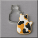 A 3 inch Quilting Cat Metal Cookie Cutter next to a decorated cat-shaped sugar cookie with a calico pattern of orange, black, and white, on a neutral gray background.