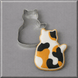 A 3 inch Quilting Cat Metal Cookie Cutter next to a decorated cat-shaped sugar cookie with a calico pattern of orange, black, and white, on a neutral gray background.