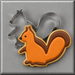 A decorated sugar cookie shaped like a squirrel in orange and brown icing, shown with a 3 inch Squirrel Metal Cookie Cutterr in the background on a gray surface.