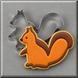 A decorated sugar cookie shaped like a squirrel in orange and brown icing, shown with a 3 inch Squirrel Metal Cookie Cutterr in the background on a gray surface.