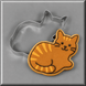 A 4 inch Cat Metal Cookie Cutter behind an orange gingerbread cookie with a cat design, shown on a gray background.
