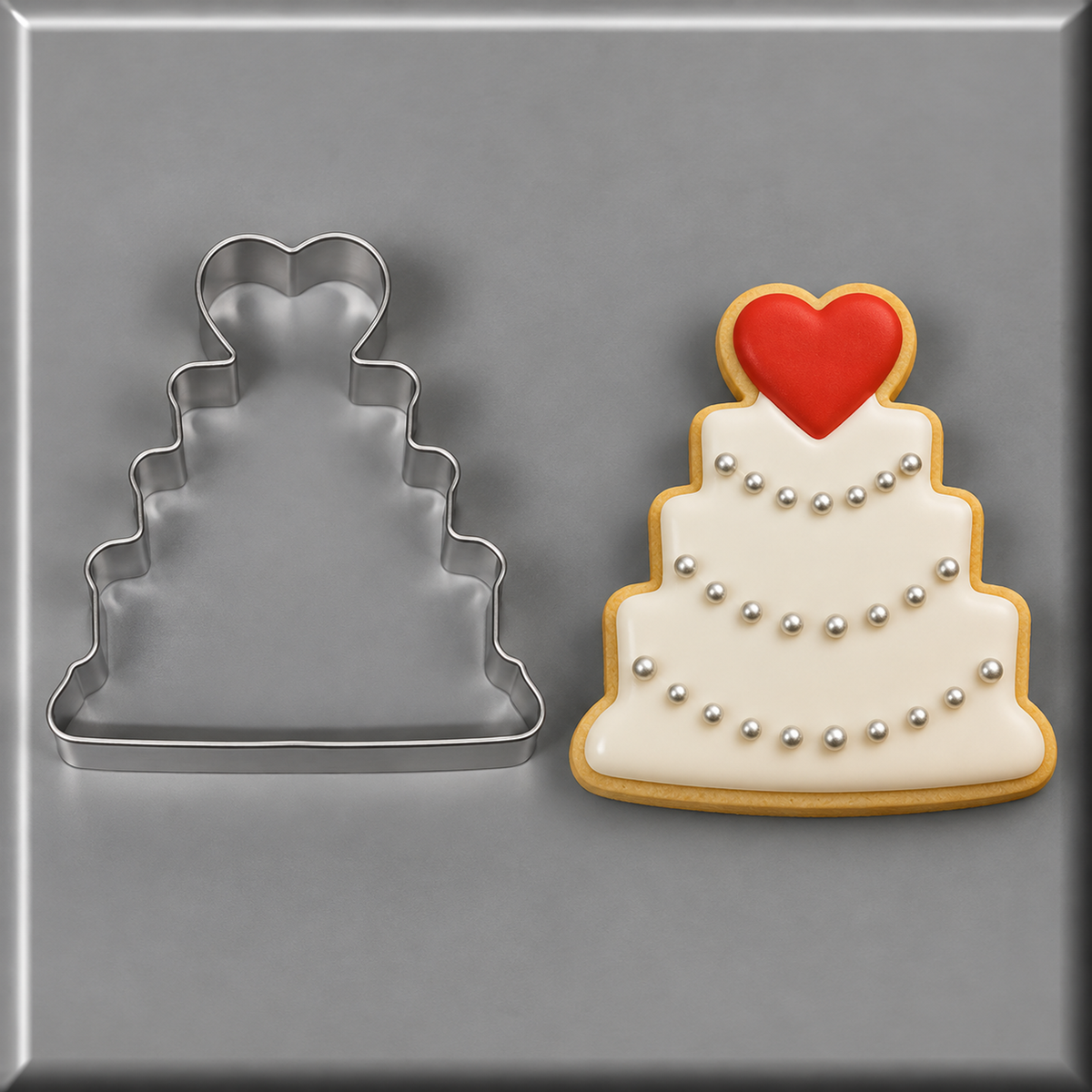  A 4.25 inch Wedding Cake Metal Cookie Cutter next to a white wedding cake cookie with heart on top