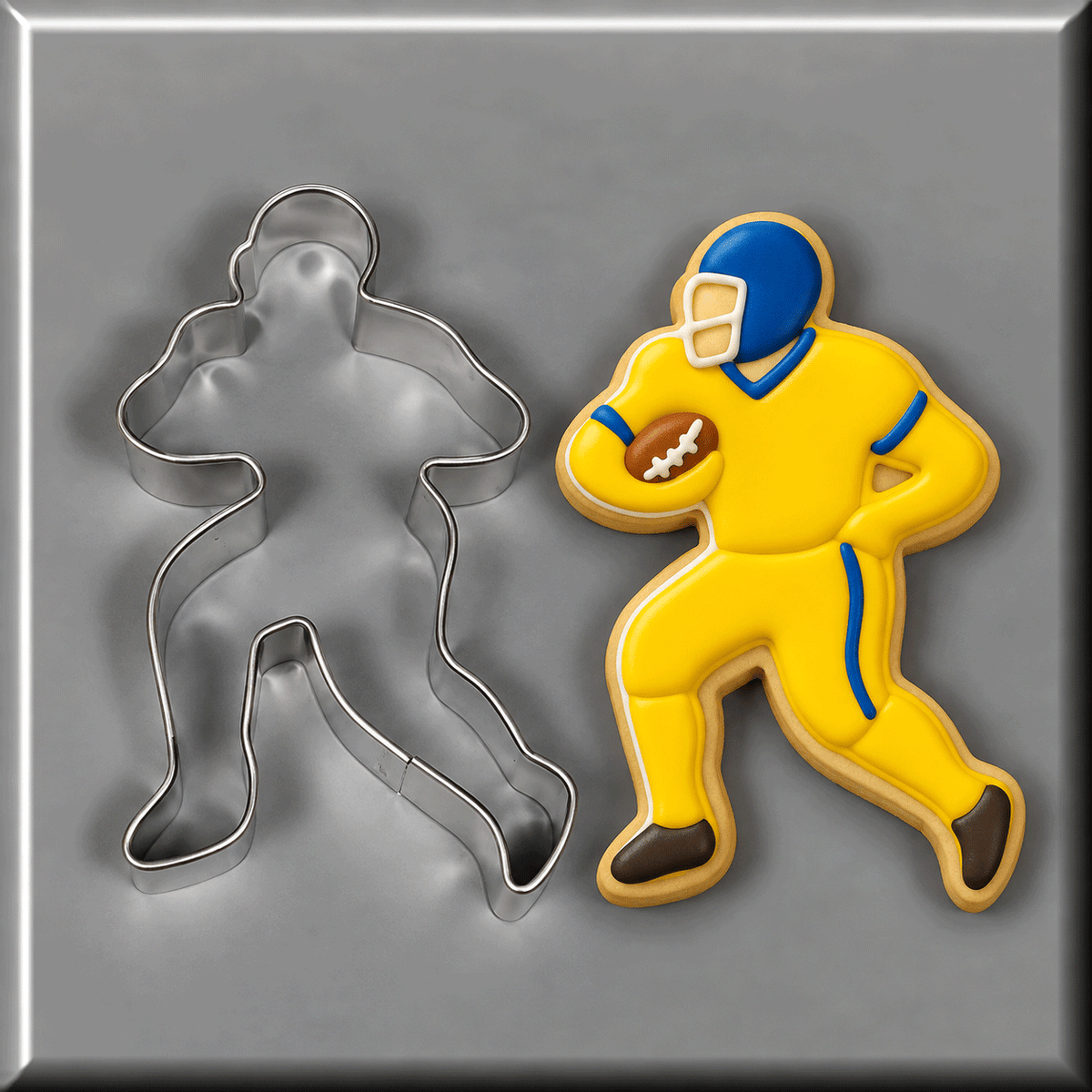 A 5 inch Football Player Metal Cookie Cutter is shown next to a decorated example cookie of the same design, featuring a yellow uniform, blue helmet, and brown football on a gray background.