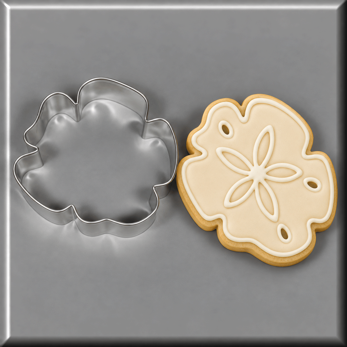 A 3.25 inch Sand Dollar Hibiscus Metal Cookie Cutter shown next to a decorated sand dollar cookie on a smooth gray surface.