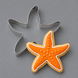 A 3.75 inch Starfish Metal Cookie Cutter placed behind an orange starfish-shaped decorated cookie on a smooth gray surface.