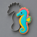 A 4 inch Seahorse Metal Cookie Cutter shown beside a decorated seahorse-shaped sugar cookie on a smooth gray background.