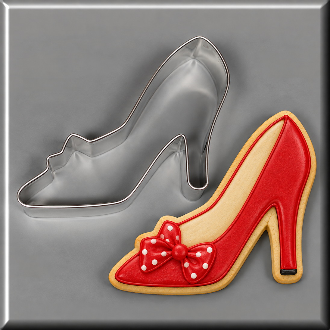 A red high-heeled shoe-shaped cookie with a white polka-dot bow and beige icing outline, shown next to a 4 inch Shoe or Slipper With Bow Metal Cookie Cutter on a gray background.