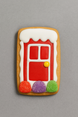 Decorative cookie shaped like a fairy door with a red door, white trim, and colorful accents on a gray background from a 2 inch Gingerbread House Door Metal Cookie Cutter