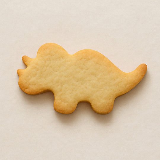 Plain triceratops-shaped cookie on a beige background from a 4 inch Triceratops Metal Cookie Cutter